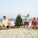 Un grupo de amigos reunidos en torno a un árbol de Navidad en la playa