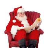 Papá Noel lee la carta de los regalos sentado en un sillón